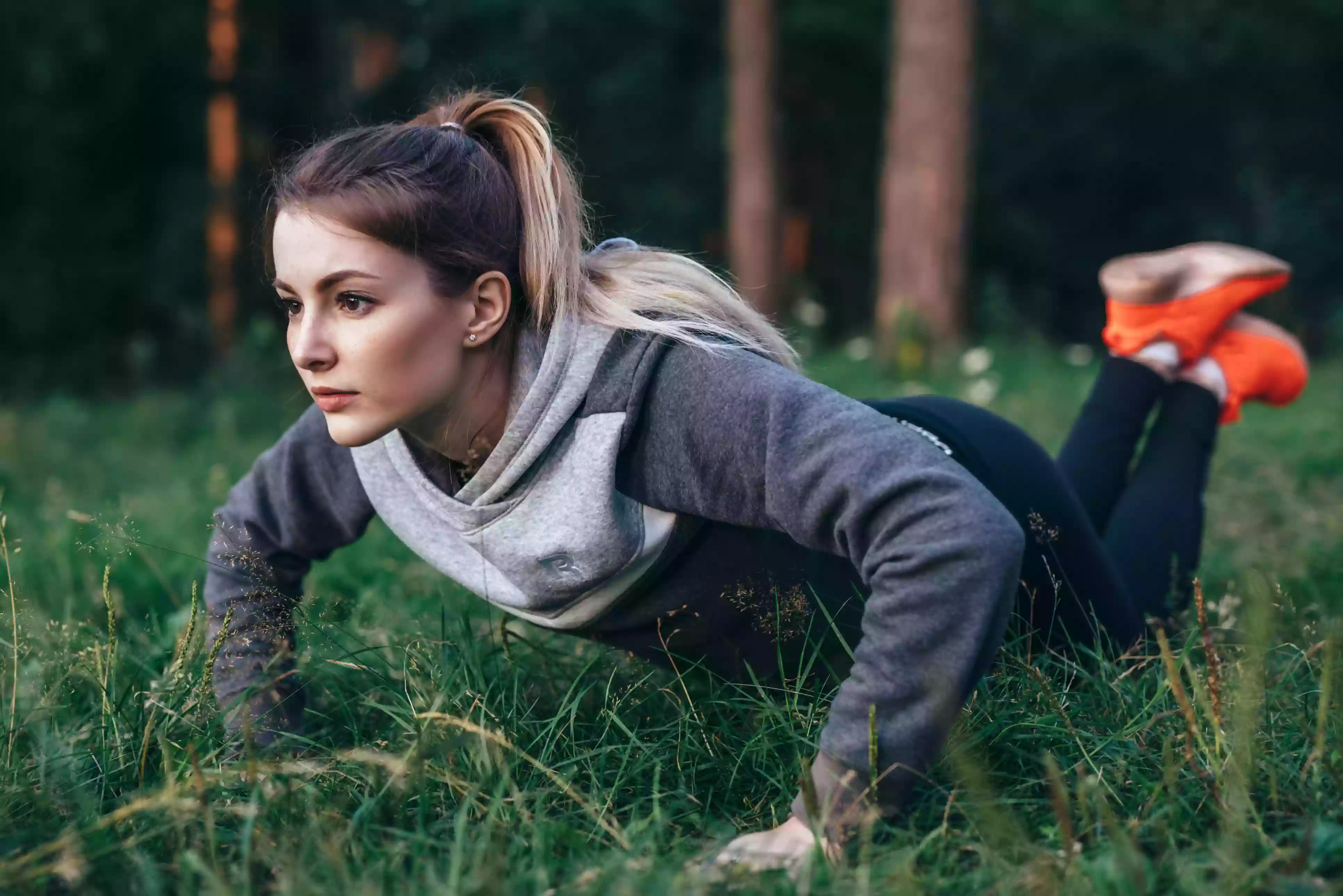 Young pretty blonde working out on grass in park doing knee push-ups